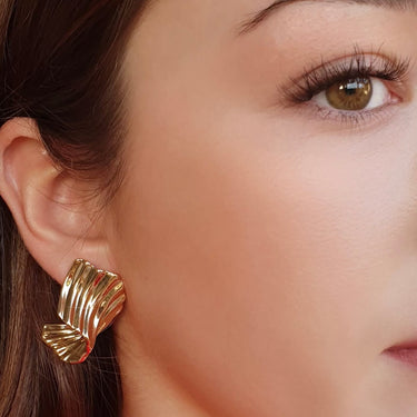 Close-up of a person wearing a gold earring with a red garment in the background