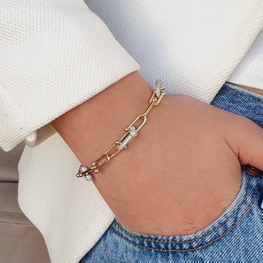 Person wearing a gold bracelet on a neutral background