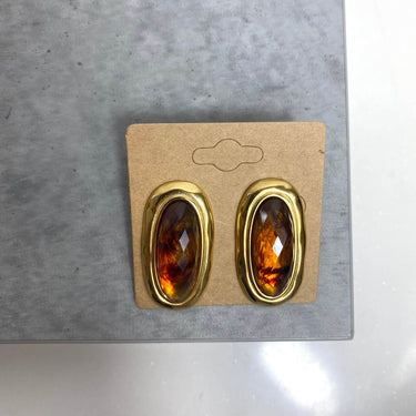 Pair of amber gemstone earrings in gold setting on a cardboard backing against a gray surface.