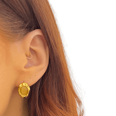 Gold earring worn by a person with brown hair on a white background