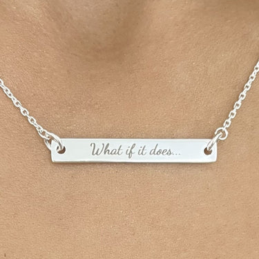 Silver necklace with engraved message on a person wearing a black lace top.
