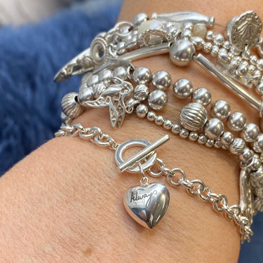 Close-up of a wrist wearing multiple silver bracelets with various charms.