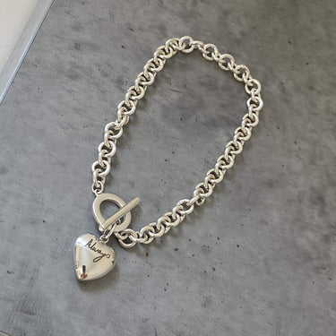 Silver chain bracelet with a heart-shaped tag on a gray surface