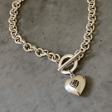 Silver chain bracelet with a heart-shaped charm featuring a rose design on a gray surface.