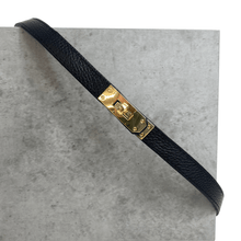 Black leather strap with a gold buckle on a gray surface