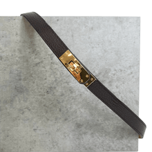 Brown leather belt with a gold buckle on a gray concrete surface
