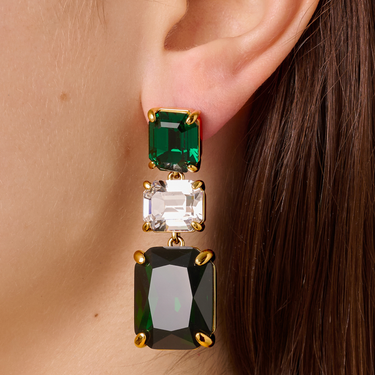 Close-up of a person wearing a set of earrings with green and clear gemstones.