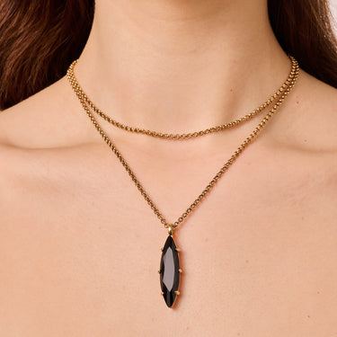 Gold necklace with a black pendant on a person's neck
