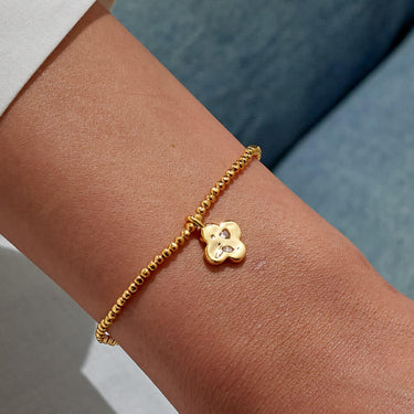 Gold bracelet with a flower charm on a wrist against a neutral background