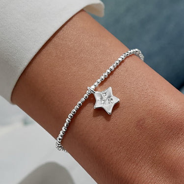 Silver bracelet with a star charm on a wrist against a blurred background