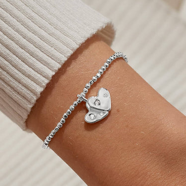Silver bracelet with a heart charm on a wrist against a neutral background