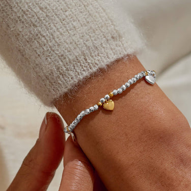 Close-up of a wrist wearing a silver bracelet with heart charm, against a neutral background.