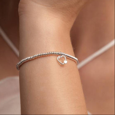 Silver bracelet with a heart charm on a wrist against a neutral background