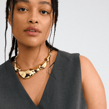Woman wearing a gold necklace against a plain background