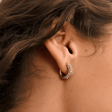Close-up of an ear wearing a gold hoop earring with small stones.