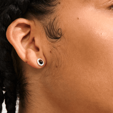 Close-up of an ear with a small round earring on a person with braided hair.
