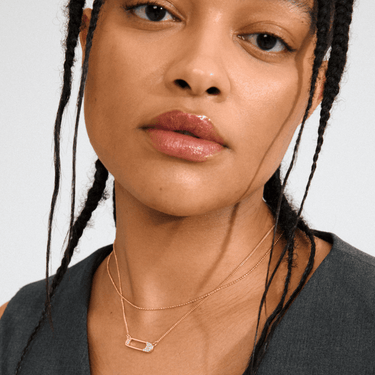 Close-up of a person wearing a gold necklace with a clear pendant on a plain background