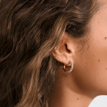Close-up of a person wearing a gold hoop earring with a blurred background