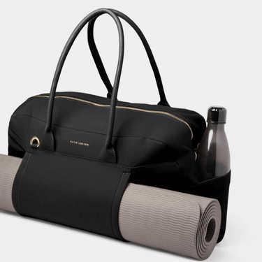Black duffel bag with yoga mat and water bottle on a light gray background