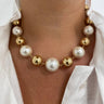 A close-up of a person wearing a pearl and gold beaded necklace. The necklace features large white freshwater pearls and polished gold spacer beads, displayed on the wearer's neck over a white collared shirt.