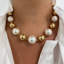 A close-up of a person wearing a pearl and gold beaded necklace. The necklace features large white freshwater pearls and polished gold spacer beads, displayed on the wearer's neck over a white collared shirt.