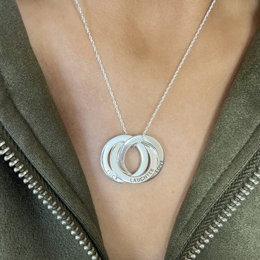 Silver necklace with a pendant worn by a person in an olive green jacket.