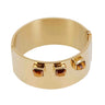 A wide gold-toned metal cuff bracelet with three square faceted brown gemstone accents on the front, shown on a plain light gray background.