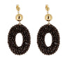 A pair of gold and black beaded dangle earrings on a light gray background with a soft reflection below.