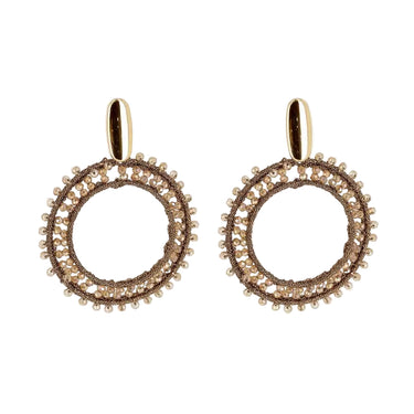 A pair of gold-toned dangle earrings with circular openwork designs, accented by small clear beads and a polished oval post, shown on a light gray background with a soft reflection below.