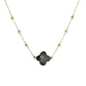 A delicate gold chain necklace featuring a central four-petal flower charm in a smoky black glass finish, suspended against a plain light gray background.