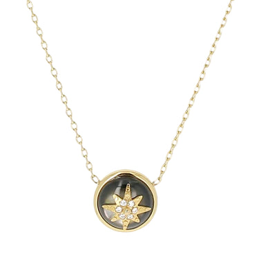 A gold chain necklace with a circular pendant featuring a dark mother-of-pearl background and a gold compass star motif with small clear crystals, shown on a light gray background.