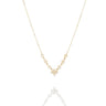 A delicate gold chain necklace featuring a V-shaped arrangement of small gold rings and a central cluster of clear stones, displayed on a light gray background with a soft reflection below.