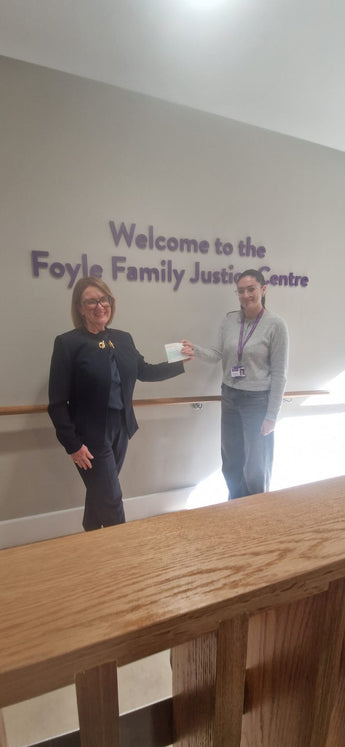 Two people standing in front of a wall with 'Welcome to the Foyle Family Justice Centre' text.