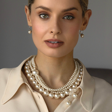 Woman wearing a pearl necklace and earrings against a neutral background