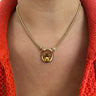 A gold chain necklace with a central gold ring and a round yellow gemstone pendant, worn on a model's neck over a bright orange knit top.