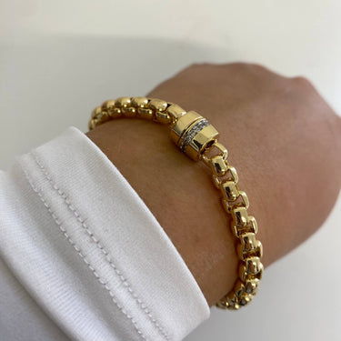 Gold bracelet on a wrist with a white background