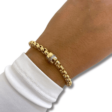 Gold bracelet on a wrist with a white sleeve against a neutral background