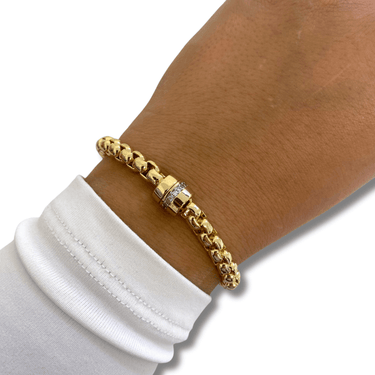 Gold bracelet on a wrist with a white sleeve against a neutral background