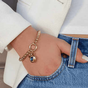 Gold bracelet with a blue gemstone on a wrist, wearing a white jacket and blue jeans.