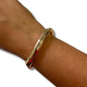 A polished gold bangle bracelet with a twisted rope detail at the clasp, shown worn on a person's wrist against a white background.