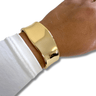 Gold bracelet on a wrist with a white sleeve against a white background
