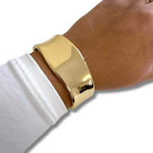 Gold bracelet on a wrist with a white sleeve against a white background