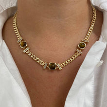 A gold-toned chain necklace with three oval brown gemstone centers and small rectangular clear stone accents, worn on a model's neck over a white collared shirt.