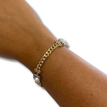 A gold-toned Cuban link chain bracelet with heart-shaped clear crystal accents, shown worn on a person's wrist against a plain white background.