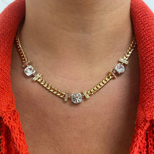 A gold chain necklace with clear crystal accents, worn on a person's neck over a bright red knit top.
