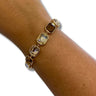 A gold-toned bracelet with faceted clear and smoky brown gemstones, shown worn on a person's wrist against a plain white background.