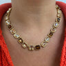 A gold-toned necklace with rectangular faceted clear and smoky brown gemstones, worn on a model's neck over a bright coral-red knit top.