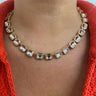 A gold-plated collar necklace featuring rectangular clear glass gems with a pink tint, worn by a model in a red knit top.