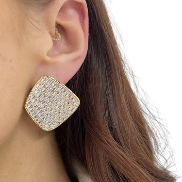 Gold and crystal earring worn by a person with brown hair.