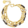 A gold-toned multi-strand bracelet featuring chunky geometric links, small gold beads, dark gray faceted beads, and white pearl accents, displayed on a clean white background.